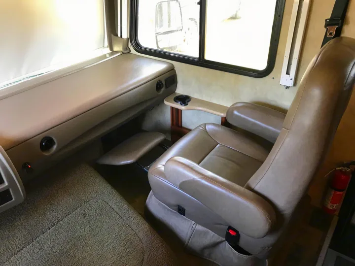 Inside a cozy RV rental: recliner chair with footrest, side table, window, and padded bench. Perfect for travel comfort.. Fleetwood Class A 2015