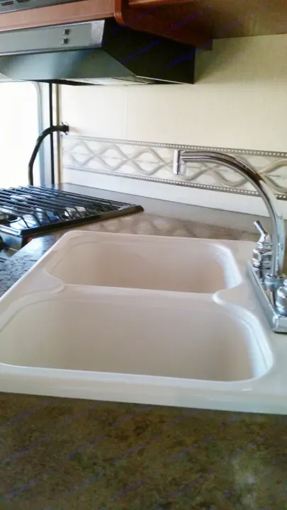 Clean RV rental kitchen with double sink, faucet, stove grate, and range hood on a speckled countertop.. Winnebago Vista 2015