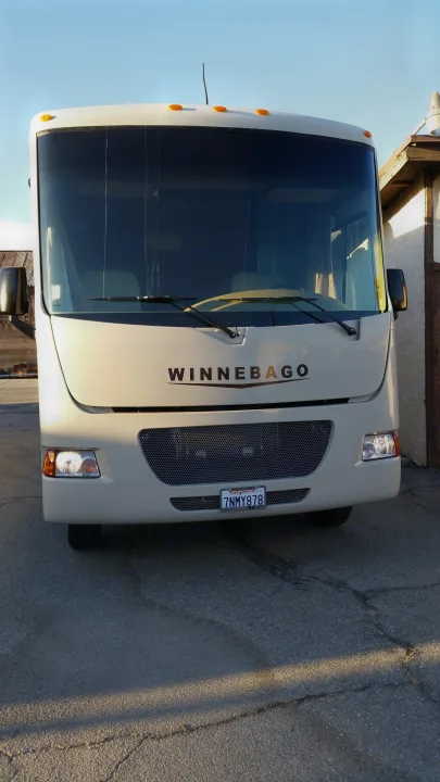 Cream Winnebago motorhome, perfect for your next rv rental. Parked on asphalt under a clear sky.. Winnebago Vista 2015