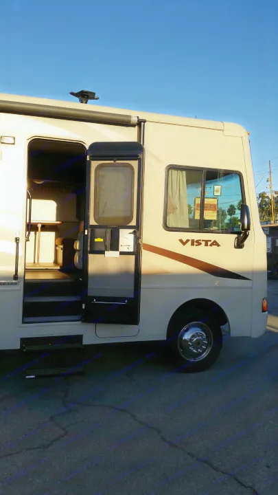 Side view of an RV rental, beige with open door showing interior steps. Sunny day on asphalt.. Winnebago Vista 2015