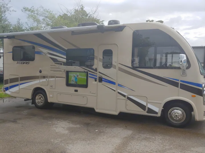 Beige Thor Vegas RV rental with an extended awning & outdoor TV playing golf. Ready for travel & camping.. Thor Motor Coach Vegas 24.1 2020