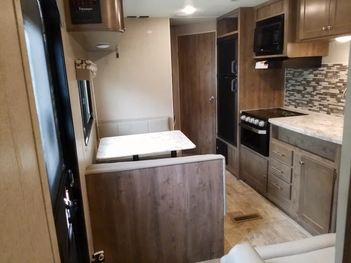 RV rental interior: Modern kitchen with stove, microwave, fridge, and a light-wood dinette with table and benches.. Dutchmen Aspen Trail 2019