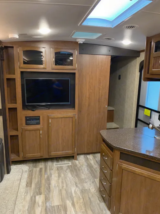 RV rental interior: wood-toned cabinets, media center with TV, kitchen counter, and patterned flooring.. Jayco White Hawk 2017