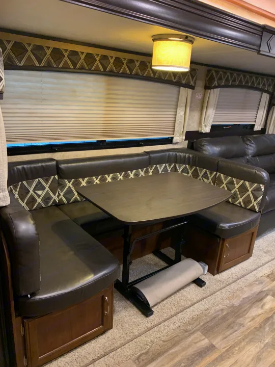 RV rental interior: U-shaped dinette with patterned cushions, table, windows, and ceiling light fixture.. Jayco White Hawk 2017