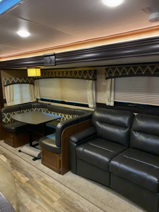 Spacious RV rental interior featuring a black leather sofa, cozy U-shaped dinette, wood-look flooring, and warm lighting.. Jayco White Hawk 2017