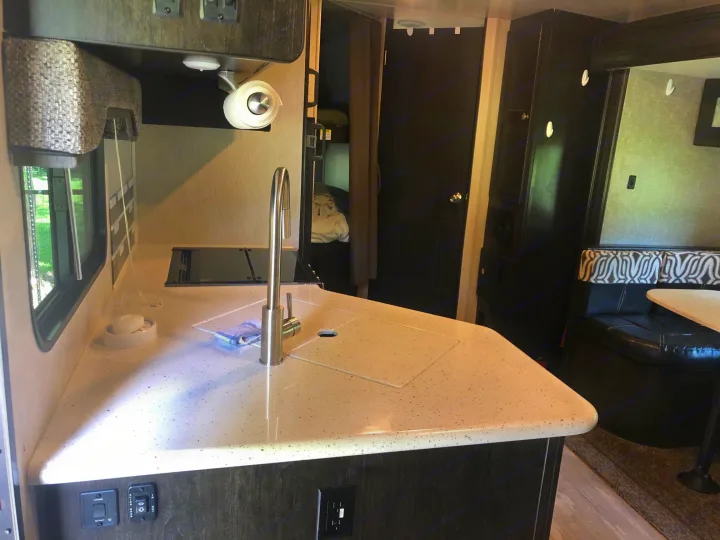 Modern RV rental kitchen with speckled countertop, sink, cooktop, and an adjacent dining booth. Ready for your trip!. Heartland North Trail 2019