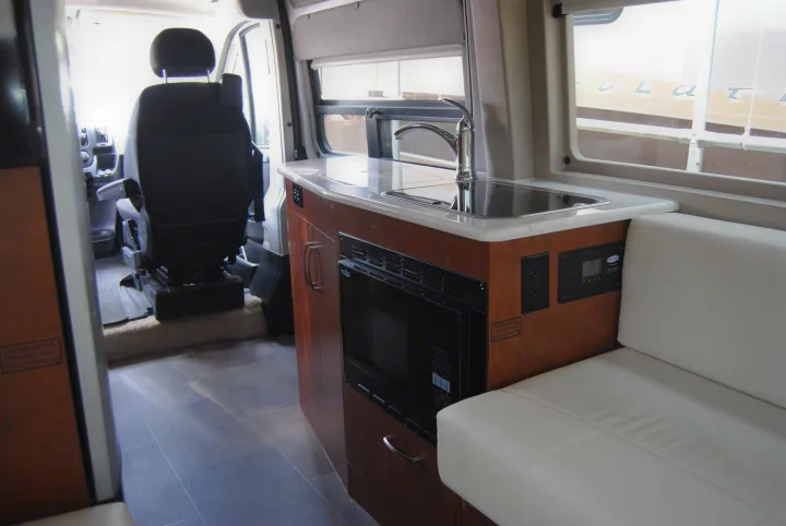 Inside an RV rental: features include a compact kitchen with sink, microwave, and cozy bench seating. Driver's area visible.. FL #44 Lexor 2020