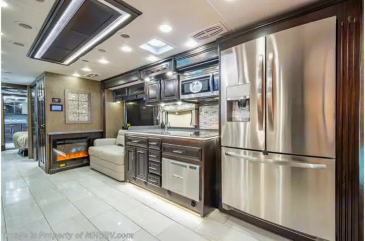 Luxury RV rental interior: spacious living area with modern kitchen, stainless steel appliances, and built-in fireplace.. Forest River Berkshire 2020