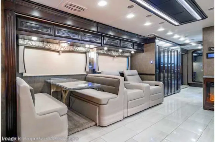 Luxury rv rental interior with light tile flooring, a cozy fireplace, dining booth, recliners, and dark wood cabinets.. Forest River Berkshire 2020