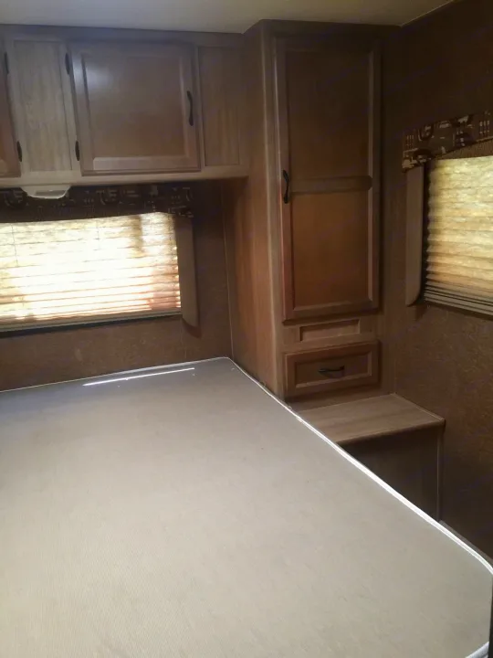 Inside an RV rental: a compact bedroom with a light-colored bed, wooden cabinets, and windows with blinds.. Coachmen Freelander 2014