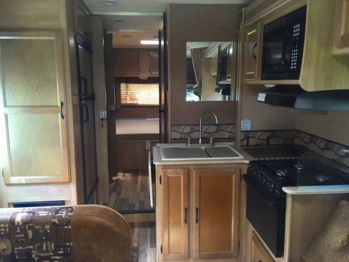 Inside this rv rental, a compact kitchen with microwave, stove, sink, and fridge, opens to a rear sleeping area.. Coachmen Freelander 2014