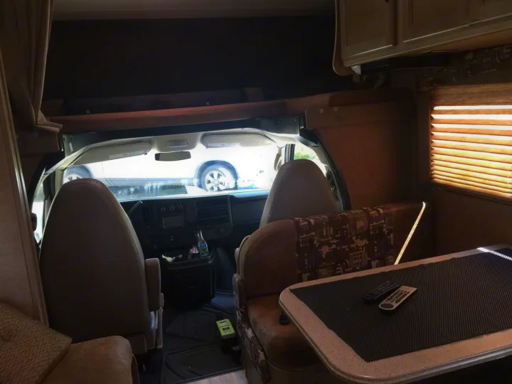 An RV rental's inviting interior features a dining booth, driver's cabin, and overhead bed.. Coachmen Freelander 2014