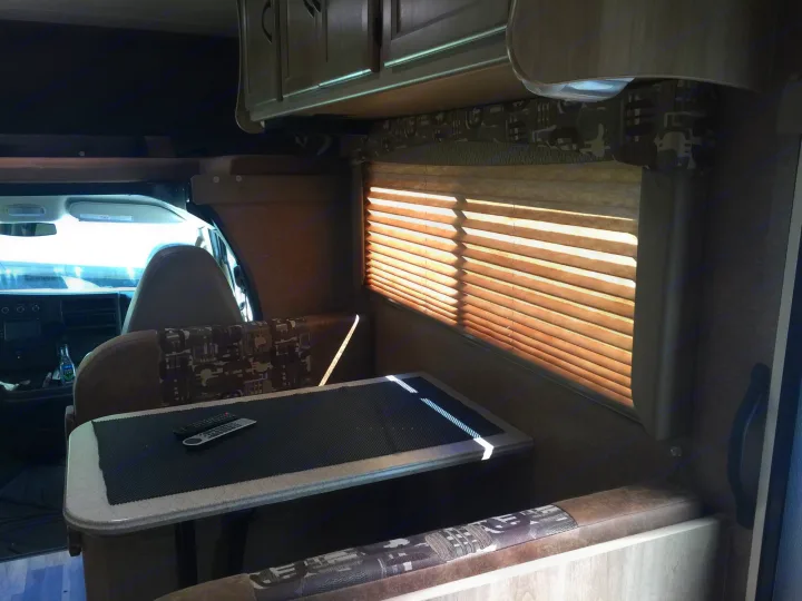 Cozy rv rental interior showing the dinette, cab, overhead cabinets, and window with blinds. Perfect for mobile living and travel.. Coachmen Freelander 2014