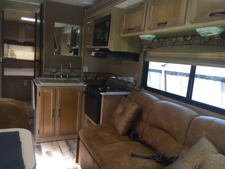 This RV rental features a full kitchen with sink, microwave, stove, and comfortable brown sofa seating area.. Coachmen Freelander 2014