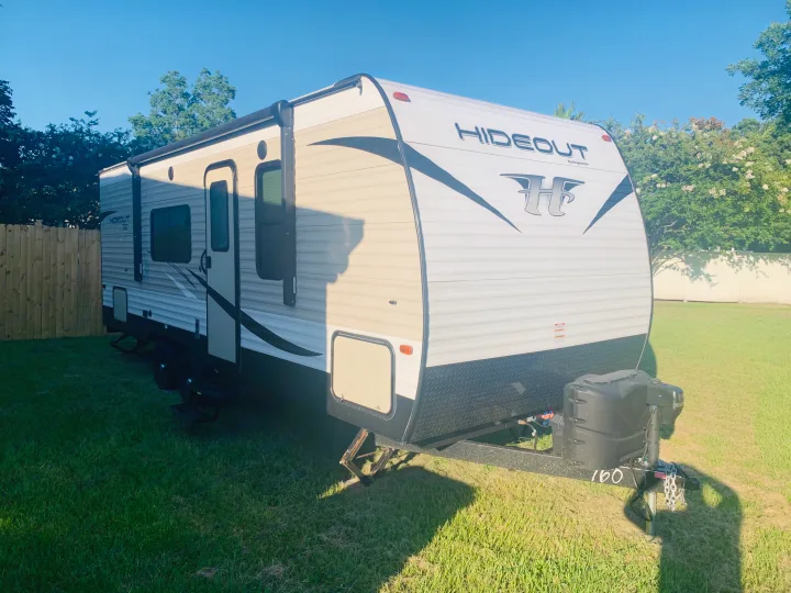 An eye-level view of a Hideout by Keystone travel trailer, ideal for an rv rental, parked on vibrant green grass.. Keystone Hideout 2019