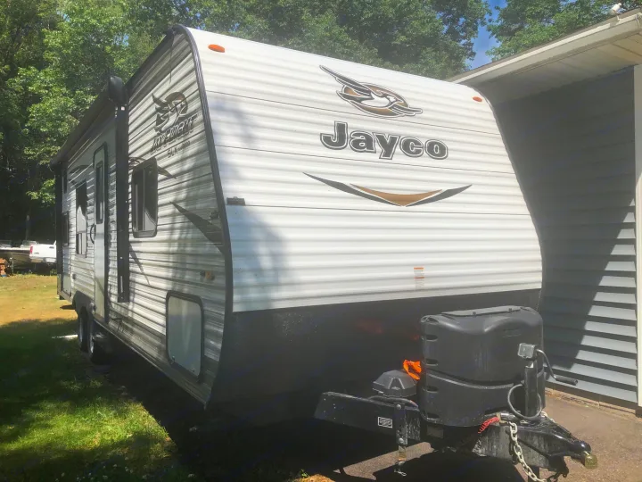 Jayco travel trailer, an excellent RV rental option. This white & black recreation vehicle shows its front with propane tanks.. Jayco Jay Flight 2018