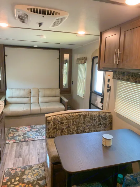 Step inside this inviting rv rental. Features a comfortable sofa, dinette, AC unit, and wood floors, making it a perfect living space.. Keystone Hideout 2019