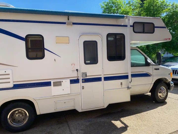 White Class C RV rental parked on concrete, featuring blue and grey stripes and a rolled-up awning.. Majestic Leisure Craft E350 2001