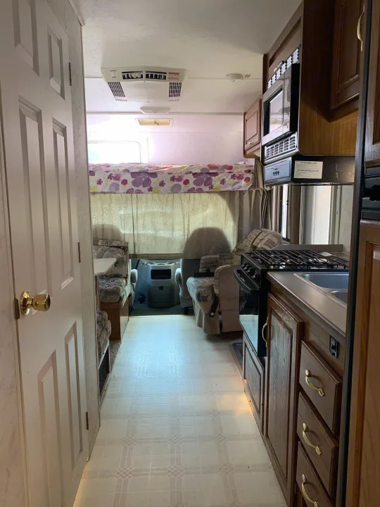 RV rental interior showcasing a kitchen, dinette, and an overhead bunk with a view towards the front of the vehicle.. Majestic Leisure Craft E350 2001