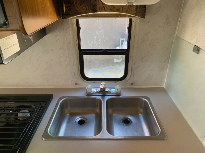 Compact rv rental kitchen: a clean stainless steel double sink, gas stove, and window providing natural light.. Majestic Leisure Craft E350 2001