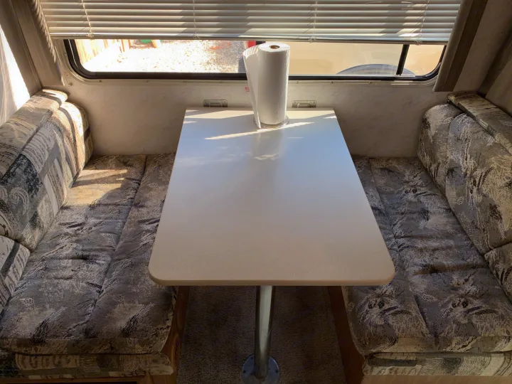 Bright RV rental dinette with a central table, two cushioned benches, and window blinds.. Majestic Leisure Craft E350 2001