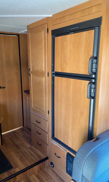 Inside this RV rental, discover the kitchen area featuring a Dometic refrigerator, wood-paneled cabinetry, and comfortable seating.. Thor Motor Coach Four Winds Majestic 2015