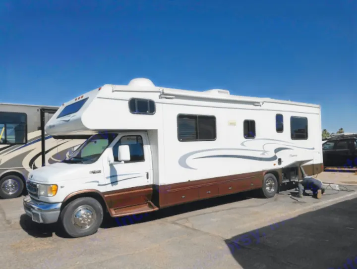 White and brown Maverick RV rental parked, with a person connecting utilities for adventure travel. Clear sky.. Georgie Boy Maverick 2006