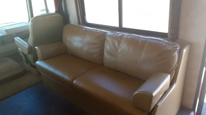 Inside an RV rental: a tan leather sofa and front passenger seat near bright windows, offering comfortable travel.. Winnebago Vista 2013