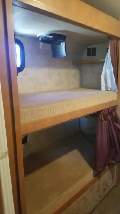 Inside an **rv rental**: two bunk beds, top one with TV and window, bottom with a privacy curtain. Ideal camper sleeping area.. Winnebago Vista 2013