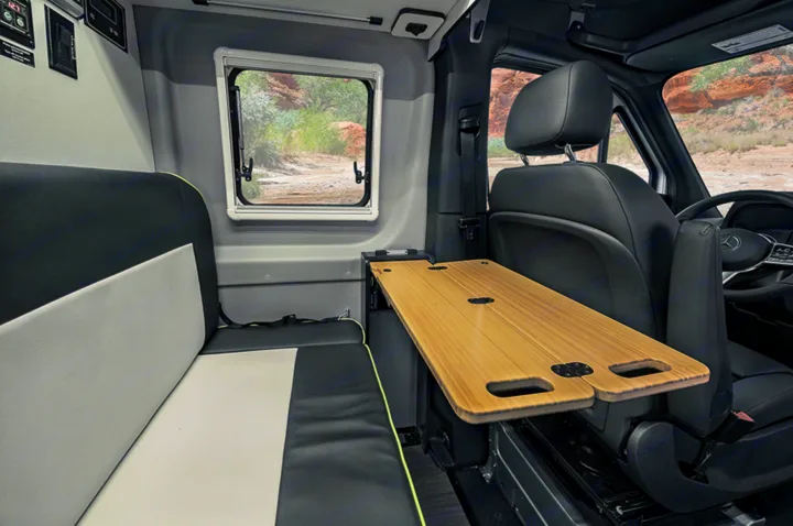 Inside an RV rental: versatile interior with bench seating, a nature-view window, and a clever swing-out wooden table.. Winnebago Revel 2020