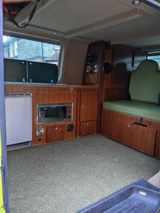 An RV rental interior featuring a kitchenette with oven, fridge, control panel, and green upholstered seating.. Volkswagen Other 2007