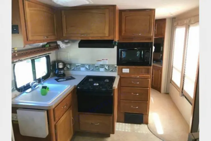 Bright RV rental kitchen with sink, stove, microwave, coffee maker, and wood cabinetry. Ready for adventure.. Fleetwood Jamboree 2007