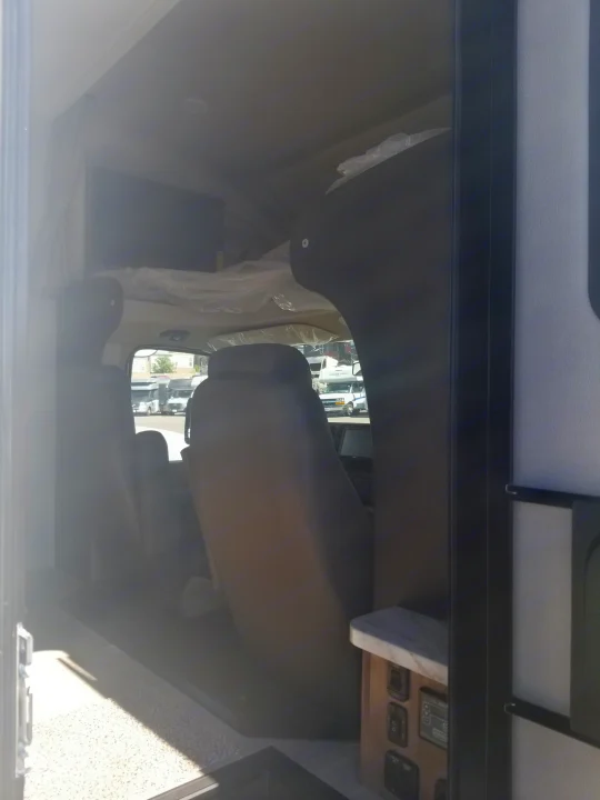 View inside an RV rental showing the front cab area with driver/passenger seats and an over-cab bunk covered in plastic.. Entegra Coach Other 2021
