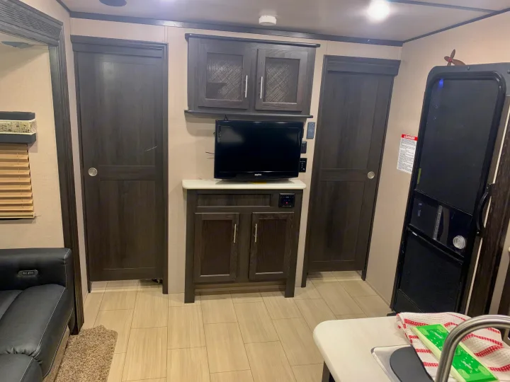 RV rental interior: A modern living space with dark wood cabinets, two doors, a TV setup, light flooring, and a kitchen counter.. Forest River X-Lite 2018