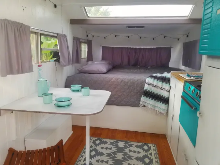 Cozy RV rental interior with a gray bed, dining table, turquoise kitchen, and skylight. Note the patterned rug and enamelware.. Custom Camper Trailer 1973