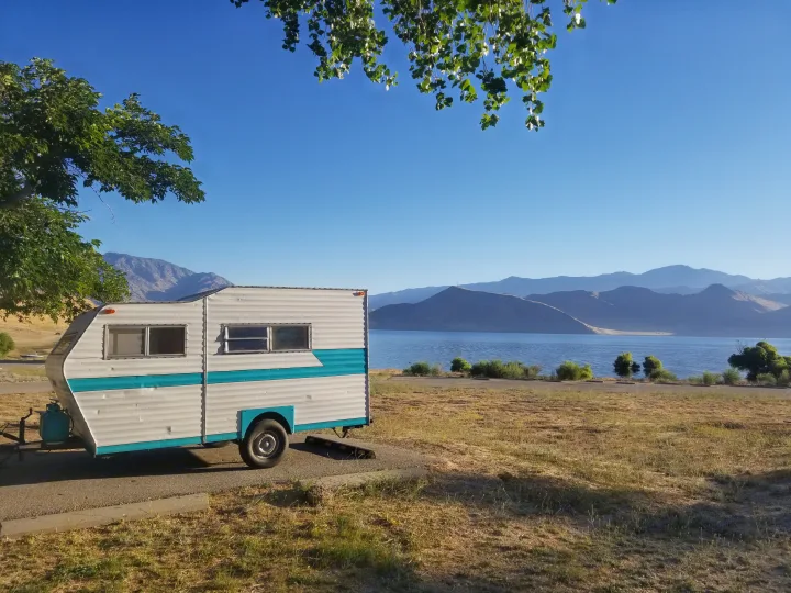 Vintage RV rental by a scenic lake with mountains, perfect for a tranquil camping trip.. Custom Camper Trailer 1973