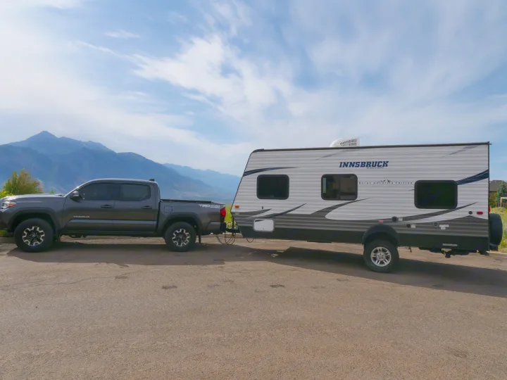 Adventure-ready RV rental! A dark grey Tacoma tows a Gulf Stream Innsbruck travel trailer against a mountain backdrop.. Gulf Stream Innsbruck 2016
