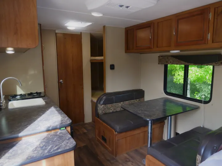 This RV rental interior shows a kitchenette with a sink and stove, a dining booth, and bunk beds, offering comfortable camper amenities.. Gulf Stream Innsbruck 2016
