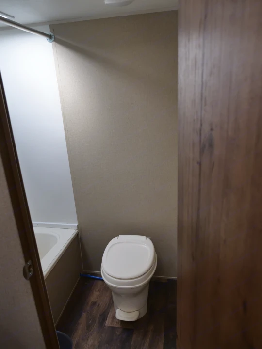 RV rental bathroom with a white toilet, shower/tub, wood-look floor, and beige walls. A compact, functional space for travel.. Gulf Stream Innsbruck 2016