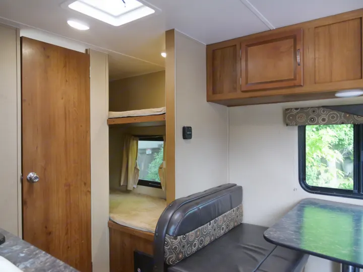 RV rental interior featuring bunk beds, a dining area with cushioned seating, and wooden overhead cabinets.. Gulf Stream Innsbruck 2016
