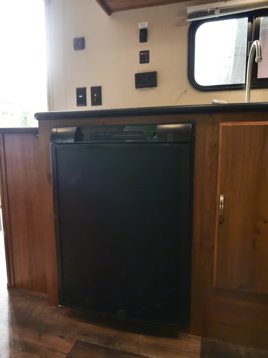 RV rental kitchen features a black built-in refrigerator, sink, faucet, and wall-mounted switches for essential amenities.. Gulf Stream Innsbruck 2016