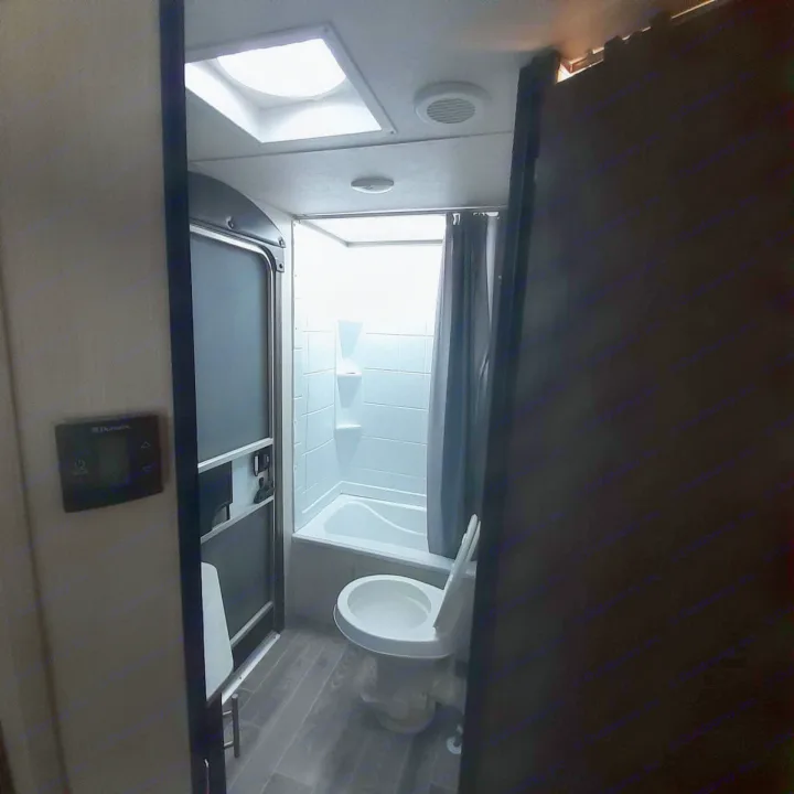 Inside an RV rental, this practical bathroom features a white toilet, shower/tub, screen door, and wall-mounted control panel.. Forest River Cherokee Grey Wolf 2019