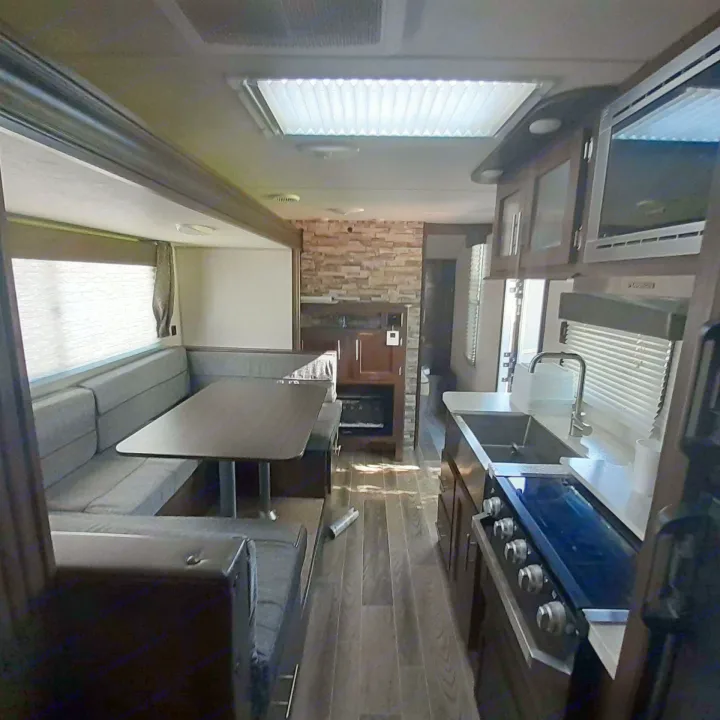 Cozy RV rental interior showing a comfortable dinette, a well-equipped kitchen with a stove and sink, and wood floors.. Forest River Cherokee Grey Wolf 2019