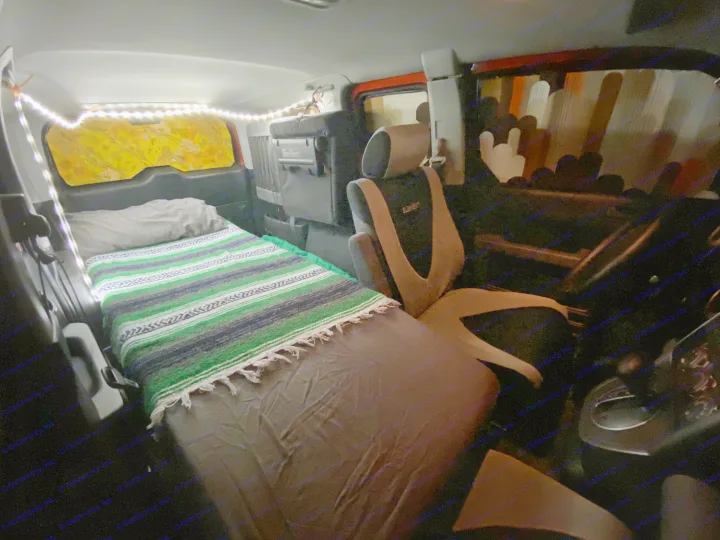 Cozy car camping interior of an RV rental, featuring a bed with a colorful blanket and string lights.. Honda Element 2005