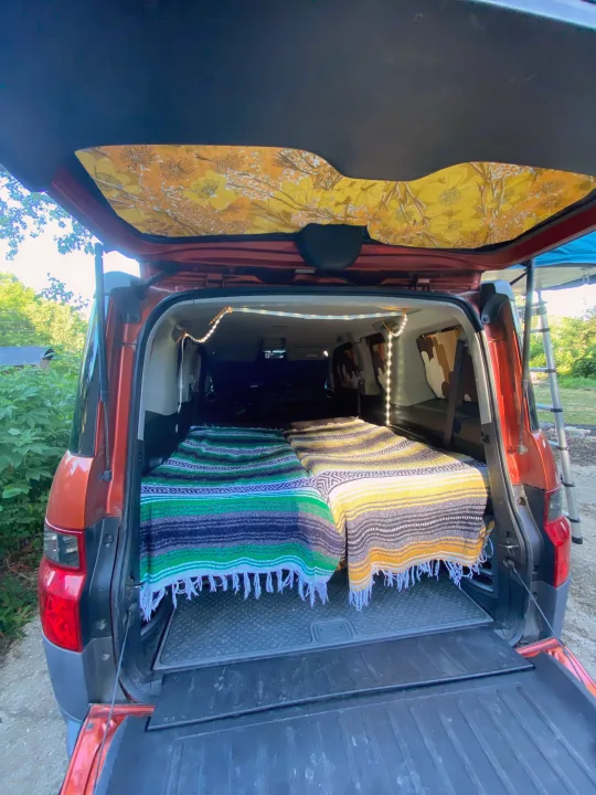 Inside a customized vehicle, two colorful blankets create a cozy sleeping setup, ideal for car camping or an RV rental road trip.. Honda Element 2005