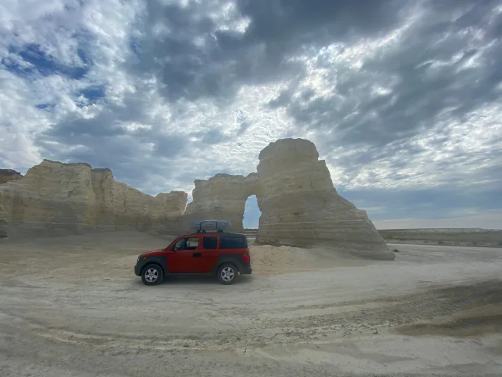 Red Honda Element with rooftop tent, resembling an RV rental, parked amidst towering white rock formations under a cloudy sky.. Honda Element 2005