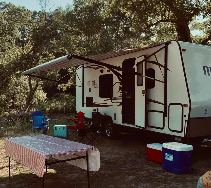 RV rental setup: A white travel trailer, awning, table, chairs, & coolers at a sunny outdoor campsite. Perfect for adventure!. Forest River Rockwood Mini Lite 2017