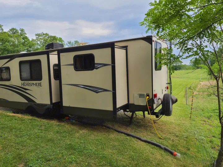 This RV rental is parked with slide-outs extended, showing power and drainage connections at a lush green campsite.. Forest River Salem Hemisphere 2015