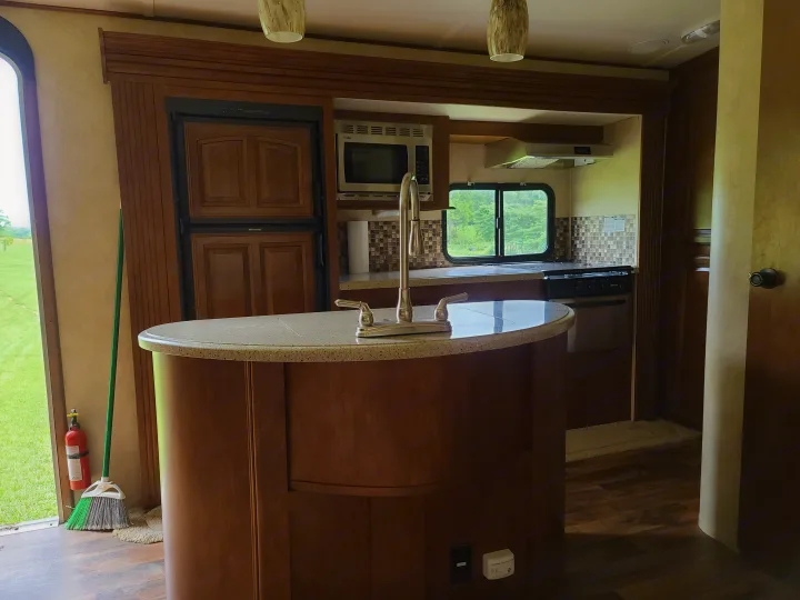 This RV rental kitchen features a central island with a sink, wood cabinets, microwave, and refrigerator for comfort.. Forest River Salem Hemisphere 2015