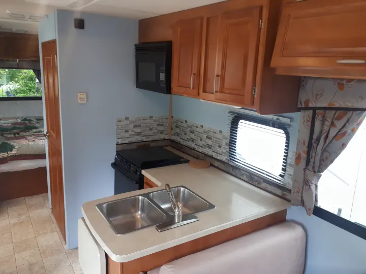 RV rental interior: bright kitchen with double sink, stove, microwave, and cabinets; a bedroom is visible.. Other Other 2009